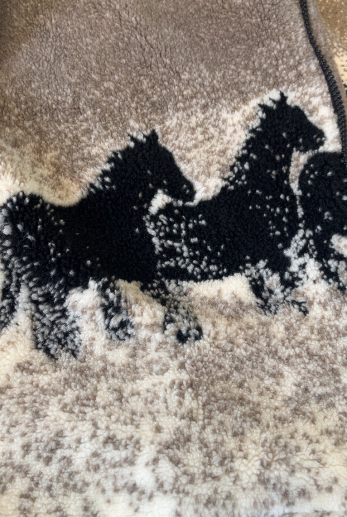 Close-up of black horse print on tan and cream sherpa jacket